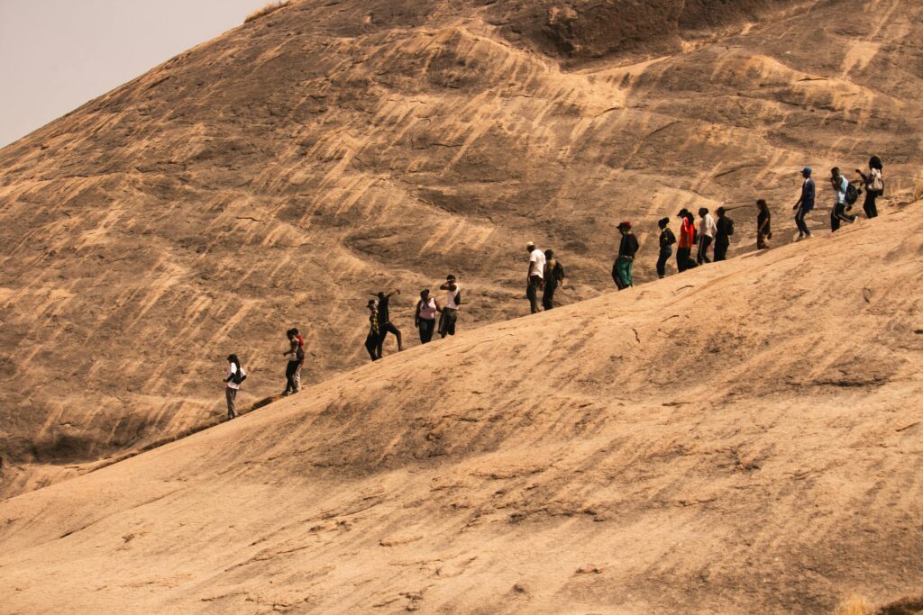 A group of hikers ascending a large rocky hill in Kaduna, Nigeria under clear skies.
